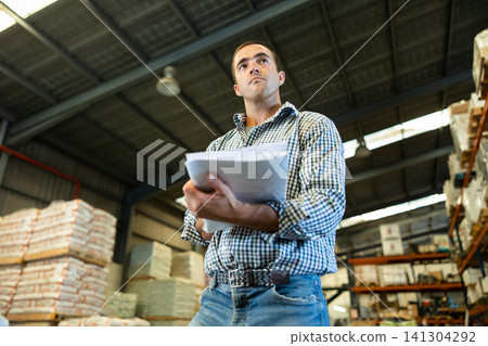 Engineer or foreman holding documents and checking inventory or job details indoor. Engineering site and working with technology concept 141304292