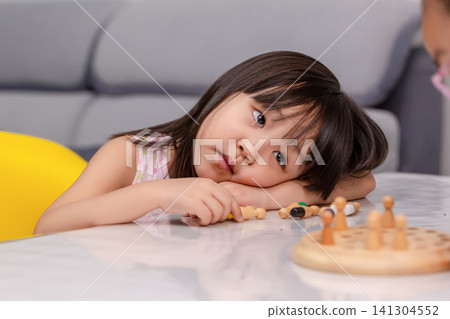 Bored and tired little Asian girl leaning her head on the table while Playing with educational toys at home. 141304552