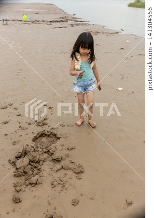 An Asian girl playing on the beach by the river in summer. An Asian girl playing on the beach by the river in summer. 141304556