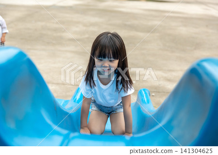 Cute Asian Girl Playing on Slide at Playground and Smiling at Camera Cute Asian Girl Playing on Slide at Playground and Smiling at Camera 141304625