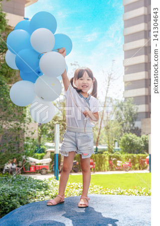 A happy Asian girl holds up a bunch of white and blue balloons outdoors. A happy Asian girl holds up a bunch of white and blue balloons outdoors. 141304643