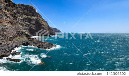 Rocky coastline with dark volcanic rocks and clear blue ocean waves lapping against the shore in a coastal landscape. High quality photo Rocky coastline with dark volcanic rocks and clear blue ocean waves lapping against the shore in a coastal landscape. High quality photo 141304802