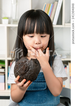 Adorable Asian girl with messy chocolate face eating chocolate cake, sweet tooth and messy eating. Adorable Asian girl with messy chocolate face eating chocolate cake, sweet tooth and messy eating. 141304848