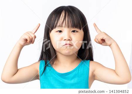 Angry little Asian girl pointing at her head with both fingers, stubborn and frustrated child. Angry little Asian girl pointing at her head with both fingers, stubborn and frustrated child. 141304852
