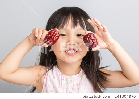 Cute Asian Little Girl Holding Red Date Fruit and Smiling Cute Asian Little Girl Holding Red Date Fruit and Smiling 141304870