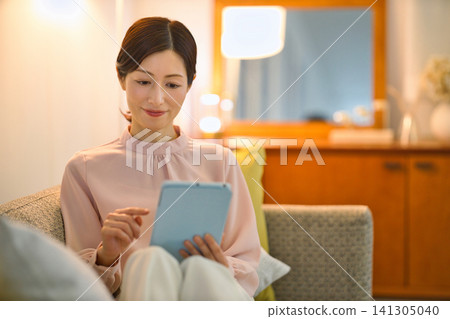 A woman in her 40s relaxing in her room at night and watching her tablet. A woman in her 40s relaxing in her room at night and watching her tablet. 141305040