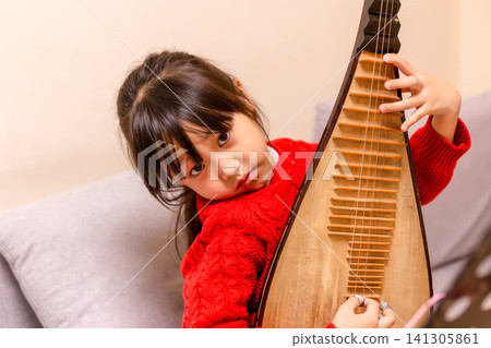 Young Chinese girl practicing Pipa traditional musical instrument on a sofa at home, creative arts and music education. 141305861