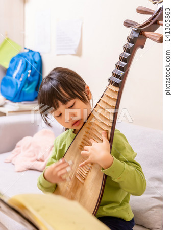 Young Chinese girl practicing Pipa traditional musical instrument on a sofa at home, creative arts and music education. Young Chinese girl practicing Pipa traditional musical instrument on a sofa at home, creative arts and music education. 141305863