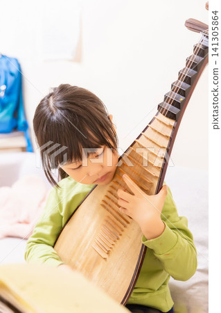 Young Chinese girl practicing Pipa traditional musical instrument on a sofa at home, creative arts and music education. Young Chinese girl practicing Pipa traditional musical instrument on a sofa at home, creative arts and music education. 141305864