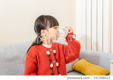 Side profile of a young Asian girl taking a big sip of milk from a clear glass cup, eyes looking into the glass Side profile of a young Asian girl taking a big sip of milk from a clear glass cup, eyes looking into the glass 141306022