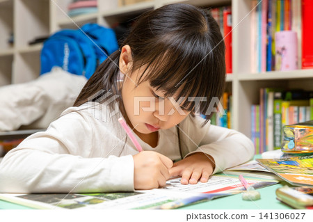 Mid shot of a focused young girl with pigtails wearing a white collared shirt, writing in a paper notebook at a study desk with bookshelves in the background. Mid shot of a focused young girl with pigtails wearing a white collared shirt, writing in a paper notebook at a study desk with bookshelves in the background. 141306027