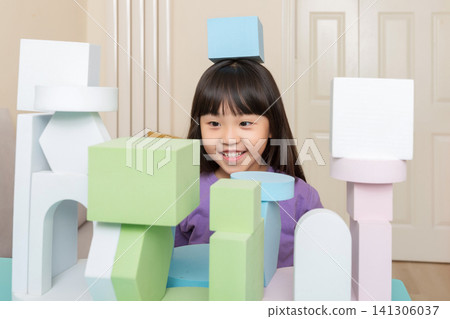 An Asian girl happily playing with foam blocks indoors. An Asian girl happily playing with foam blocks indoors. 141306037