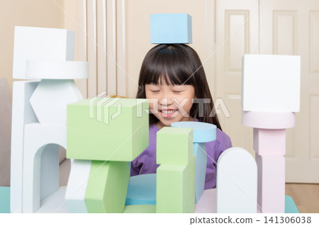 An Asian girl happily playing with foam blocks indoors. An Asian girl happily playing with foam blocks indoors. 141306038
