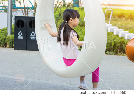 Full length shot of a young girl from behind, swinging upwards on an empty suspended plastic circle swing at an outdoor park Full length shot of a young girl from behind, swinging upwards on an empty suspended plastic circle swing at an outdoor park 141306063