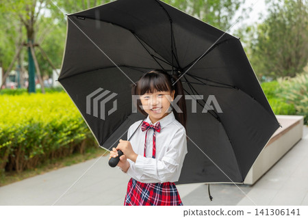 A smiling school girl holding a large black umbrella outdoors on a path. A smiling school girl holding a large black umbrella outdoors on a path. 141306141