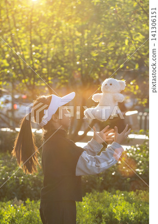Cheerful little girl playing with teddy bear in park at sunset with golden sunlight Cheerful little girl playing with teddy bear in park at sunset with golden sunlight 141306151