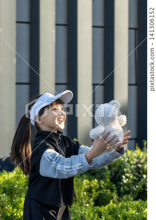 A young girl catching a white plush bear toy thrown in the air outside. A young girl catching a white plush bear toy thrown in the air outside. 141306152