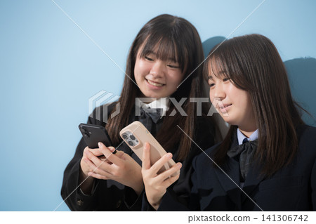 Two Japanese middle school and high school girls looking at their smartphones: sharing information and discussing safe usage. Two Japanese middle school and high school girls looking at their smartphones: sharing information and discussing safe usage. 141306742