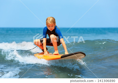 Happy young surfer girl with surfboard have fun on beach, riding on small ocean waves. Summer adventures, active families, parents and kids lifestyle, sports activities on school holiday with kids Happy young surfer girl with surfboard have fun on beach, riding on small ocean waves. Summer adventures, active families, parents and kids lifestyle, sports activities on school holiday with kids 141306890