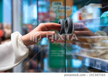 A Close-Up of a Hand Reaching for a Glass Door in a Grocery Setting, Capturing the Moment of Selection in a Modern Retail Environment A Close-Up of a Hand Reaching for a Glass Door in a Grocery Setting, Capturing the Moment of Selection in a Modern Retail Environment 141307383