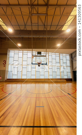 Wide symmetrical perspective of a modern indoor basketball gymnasium with polished wood floor and glass facade Wide symmetrical perspective of a modern indoor basketball gymnasium with polished wood floor and glass facade 141309563