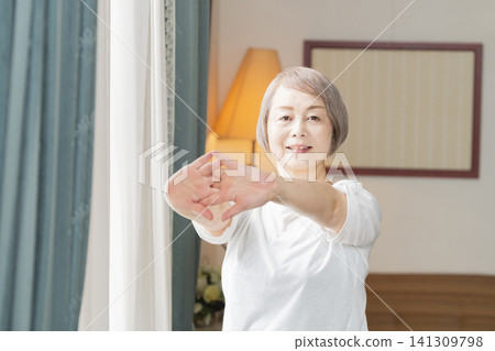 A senior woman doing morning stretches by the living room window. 141309798