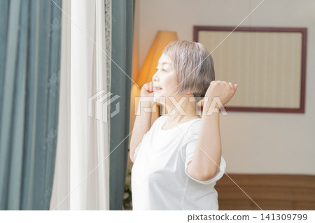 A senior woman doing morning stretches by the living room window. A senior woman doing morning stretches by the living room window. 141309799