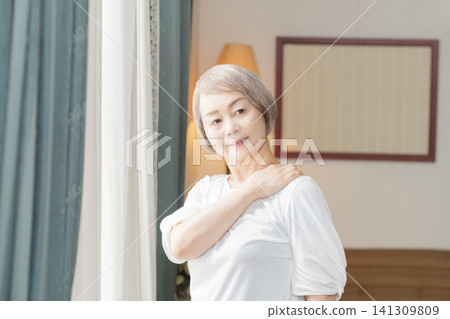 一位老婦人在客廳窗邊做晨間伸展運動。 一位老婦人在客廳窗邊做晨間伸展運動。 141309809