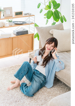 一位時尚女士坐在沙發前，正在用智慧型手機通話。 141310195