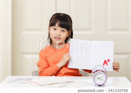 A smiling little girl shows off her A+ grade workbook, with homework assignments including words like "forgot" and "quarter". A smiling little girl shows off her A+ grade workbook, with homework assignments including words like "forgot" and "quarter". 141310708
