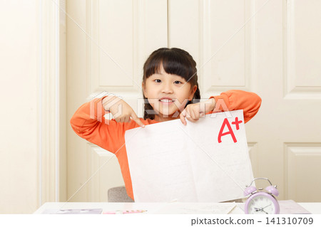 A smiling little girl shows off her A+ exam paper. A smiling little girl shows off her A+ exam paper. 141310709