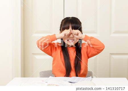 Frustrated little girl rubbing her eyes while crying over difficult school homework. Frustrated little girl rubbing her eyes while crying over difficult school homework. 141310717