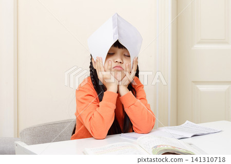 Exhausted young student resting her head with a book over her forehead in frustration. Exhausted young student resting her head with a book over her forehead in frustration. 141310718