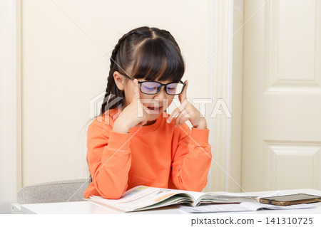 Studious girl adjusting her glasses while concentrating deeply on an open textbook. Studious girl adjusting her glasses while concentrating deeply on an open textbook. 141310725