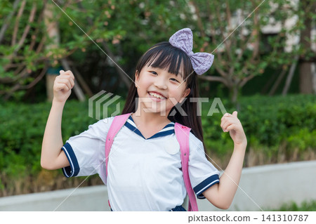 Excited Asian schoolgirl celebrating success with raised fists outdoors, motivation and achievement concept 141310787