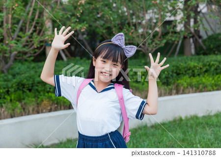 Happy Asian schoolgirl waving hands outdoors, cheerful childhood and school life concept Happy Asian schoolgirl waving hands outdoors, cheerful childhood and school life concept 141310788