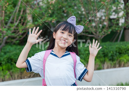 Happy Asian schoolgirl waving hands outdoors, cheerful childhood and school life concept Happy Asian schoolgirl waving hands outdoors, cheerful childhood and school life concept 141310790