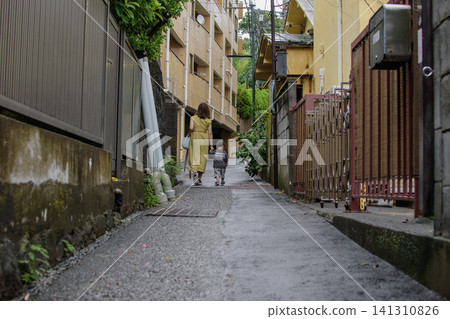 A parent and child strolling down a narrow alleyway after the rain. A parent and child strolling down a narrow alleyway after the rain. 141310826