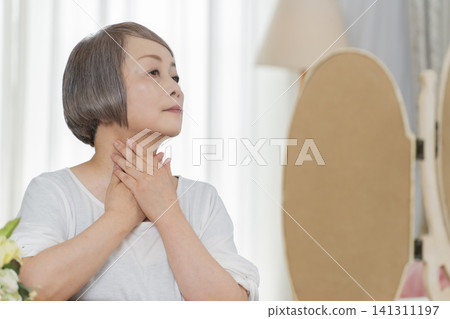 一位老婦人對著鏡子整理儀容。 一位老婦人對著鏡子整理儀容。 141311197