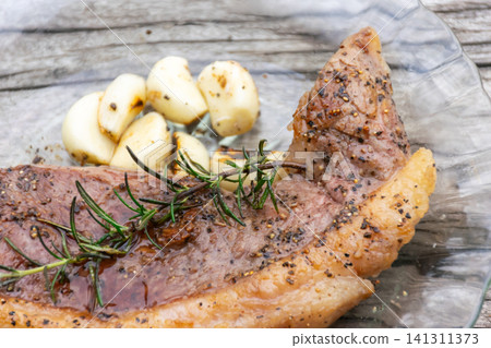 Juicy grilled beef steak seasoned black pepper rosemary roasted garlic served glass plate Fresh herbs enhance rich flavor for gourmet dining Juicy grilled beef steak seasoned black pepper rosemary roasted garlic served glass plate Fresh herbs enhance rich flavor for gourmet dining 141311373