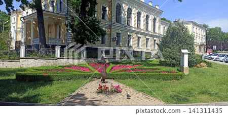 Beautiful flower bed shaped like a peacock tail in a park near a historic building Beautiful flower bed shaped like a peacock tail in a park near a historic building 141311435