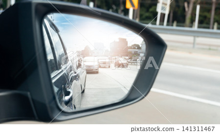 View through a car's side mirror. Focus on the side of the car. Showing other vehicles moving along a highway. Perspective captures the flow of traffic and the surroundings during a commute in city. View through a car's side mirror. Focus on the side of the car. Showing other vehicles moving along a highway. Perspective captures the flow of traffic and the surroundings during a commute in city. 141311467