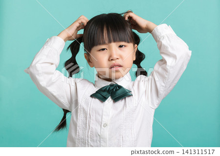 A frustrated young schoolgirl scratching her head with both hands while wearing a green bow tie and looking confused. A frustrated young schoolgirl scratching her head with both hands while wearing a green bow tie and looking confused. 141311517