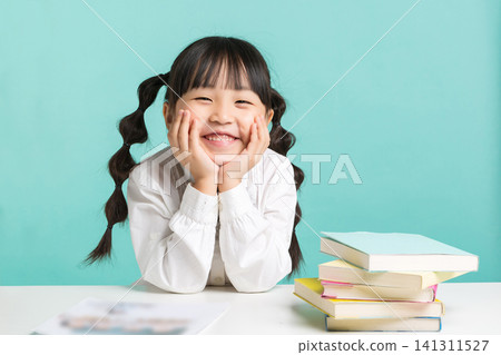 A sweet little schoolgirl leaning her chin on both hands while sitting at her study table with colorful books. A sweet little schoolgirl leaning her chin on both hands while sitting at her study table with colorful books. 141311527