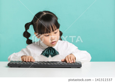 A focused elementary school student typing or practicing on a black computer keyboard placed on her white desk. 141311537