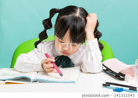 A stressed young girl resting her head on her hand while struggling with a difficult textbook assignment at her desk. A stressed young girl resting her head on her hand while struggling with a difficult textbook assignment at her desk. 141311543
