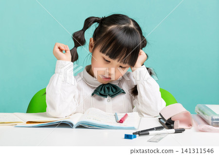 A stressed young girl resting her head on her hand while struggling with a difficult textbook assignment at her desk. A stressed young girl resting her head on her hand while struggling with a difficult textbook assignment at her desk. 141311546