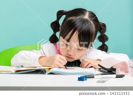 A cute little Asian girl is diligently doing her homework with her head down. A cute little Asian girl is diligently doing her homework with her head down. 141311551
