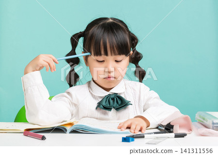 A thoughtful young student holding a pencil to her forehead while contemplating an answer to her schoolwork. A thoughtful young student holding a pencil to her forehead while contemplating an answer to her schoolwork. 141311556