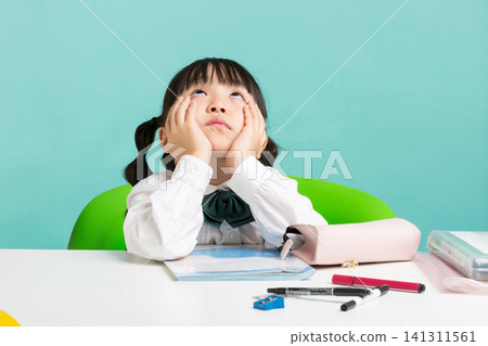 A fatigued elementary school girl holding both cheeks with her hands and looking down sadly at her open notebook. A fatigued elementary school girl holding both cheeks with her hands and looking down sadly at her open notebook. 141311561